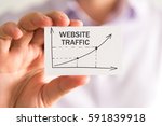 Closeup on businessman holding a card with WEBSITE TRAFFIC rising arrow and chart, business concept image with soft focus background