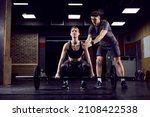 A young strong sportswoman lifting weights in gym with her personal trainer.