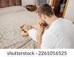 Small photo of A silly father is playing peek a boo with his daughter at home while she lying down on the bed.