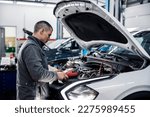 A car workshop worker is doing car battery diagnostics with special device.