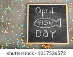 Small photo of Chalkboard with phrase "April fish day" and confetti on grey background