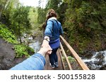 People walking across wooden bridge through mountain river. Follow me concept