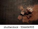 Broken chocolate pieces and cocoa powder on wooden background