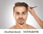 Surgeon drawing marks on male face against gray background. Plastic surgery concept