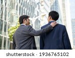 Small photo of asian corporate executive giving subordinate a pat on the back while walking in street of central business district of modern city
