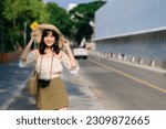 Portrait of young asian woman traveler with weaving hat and basket and a camera on green public park nature background. Journey trip lifestyle, world travel explorer or Asia summer tourism concept.