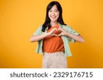 Small photo of Close up of Asian woman 30s wearing orange shirt showing heart hand gesture, symbolizing warmth and affection. Perfect for expressing love and spreading positive vibes in various projects.