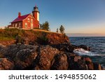 Early morning sunrise illuminates the rocks and front of Eagle Harbor Light on the Keweenaw Peninsula in Michigans Upper Peninsula. Waves from Lake Superior wash against the rocks.