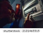 Energy crisis. Man in complete darkness holding a phone to investigate a home fuse box during a power outage. Blackout concept.