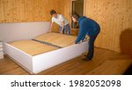 Small photo of CLOSE UP: Young couple works together to assemble a large bed in their brand new CLT home. Caucasian man and woman mount bunkie boards onto the bed frame of a large bed in their brand new bedroom.