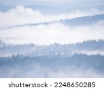 Stunning views of multi-layered forested hilly landscape created by winter mist. Silhouettes of forest treetops peeking through layers of mist in wintertime. Majestic winter view at the countryside.