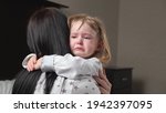 Child is crying in room in the arms of his mother. A loving young mother hugs and comforts her little daughter. Mom calms child. Family mother and baby with tears in their eyes emotionally embrace