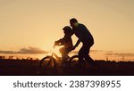 Small photo of Father helps his daughter ride bike. Father teaches child wearing safety helmet to ride bicycle in park. Child rides bicycle. Kid, dad play together, sunset. Child dream learns to ride bicycle. Family