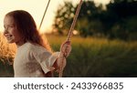 Small photo of Child plays on wooden swing, dreams of fly. Child swing, kid girl smile in flight. Child girl Happiness dream entertainment. Happy little girl swings on swing in park under tree at sunset. Family walk