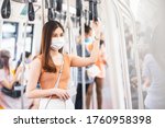 Young Asian woman passenger wearing surgical mask and listening music via smart mobile phone in subway train when traveling in big city at Covid19 outbreak, Infection and Pandemic concept