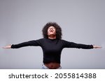 Joyful exuberant young Black woman celebrating with open arms and her head thrown back with a beaming smile over a grey studio background with copyspace
