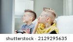 Small photo of Young brothers playing video games watching in trepidation pursing their lips in anticipation in a close up side portrait indoors at home