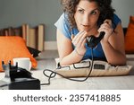Small photo of Lounging on the floor amidst cushions, a woman excitedly whispers into a vintage black phone. Amidst the pleasure of gossip, she's oblivious to the fact she'll be discussed next in the rumor mill
