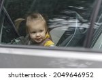 Cute and lovely toddler girl, sitting on a backseat, looking through a car window