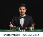 Small photo of Asian man dealer or croupier shuffles poker cards betting in casino on black background of green table, Dealer man invitation bet playing cards. Casino, poker, poker game concept.