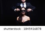 Small photo of beautiful woman in mask and man in a suit. Couple over black background. Adorable, elegant girl seducing her handsome boyfriend