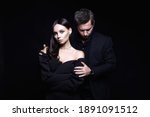 Small photo of beautiful woman in evening dress in the hands of man in a suit. Couple over black background. Adorable, elegant girl seducing her handsome boyfriend
