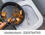 Small photo of a hand with a pan throwing spoiled meat and potato into a toilet