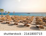 Beautiful empty beach with sun umbrellas and sunbeds. Perfect summer vacation destination. Straw sunshades and sunbeds on the empty beach with blue sea on background