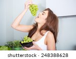 Happy young woman eating grapes in a kitchen