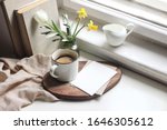 Cozy Easter spring still life. Greeting card mockup scene. Cup of coffee, books, wooden cutting board, milk pitcher and vase of flowers on windowsill. Floral composition. Yellow daffodils and tulip. 
