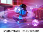 Child girl wearing virtual reality headset and looking at digital space system with planets or Universes. Space exploration with augmented reality glasses. She is sitting on flor at childroom.