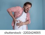 Small photo of Young man is experiencing severe pain in the abdominal cavity, he holds on to the sore spot with hands and screams.