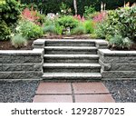 Small photo of Block retaining wall in gray color with integrated staircase into existing garden landscaped with perennial flowers and shrubs background