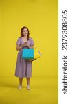 Small photo of Young woman with shopping bags uses smartphone. A woman looks through lucrative offers, promotions, and makes an online order. Full length redhaired woman in studio on yellow background. Vertical shot