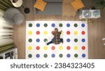 Small photo of Top view of the bright room, twister game laying on the floor, kid playing, stepping on colorful areas with hands and legs.