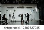 Small photo of Professional filming pavilion with a white cyclorama. Shooting of a girl in a red dress who sings into a retro microphone. Director, Cameraman and crew in Backstage.