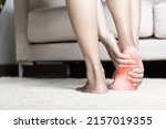 Foot pain, Asian woman standing feeling pain in her foot at home, female suffering from feet ache use hand massage relax muscle from soles in home interior, Healthcare problems and podiatry medical