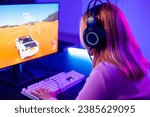 Small photo of Happy Gamer endeavor plays online video games tournament with computer with neon lights, Young player woman wearing gaming headphones intend to do playing car games online at home, Back view