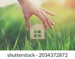 Hand holding small wooden house in green grass, safe, sweet and eco accommodation concept, shelter, home loan and insurance, family life 