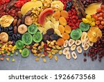 Small photo of Dried fruits and berries on gray background top view. Lemons, oranges, bananas, raisins, cranberries, kiwi, cherries, ginger, plums, strawberries, dried apricots, tangerines, dates, pineapples, figs