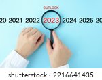 Human's hand  focused on 2023 with OUTLOOK word with magnifying glass