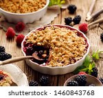 Small photo of Crumble, Mixed berry (blackberry, raspberry) crumble, stewed fruits topped with crumble of oatmeal, almond flour, butter and sugar in a baking dish on a wooden table, close-up