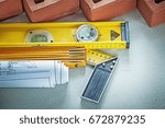 Small photo of Red bricks construction level wooden meter blueprints square rul