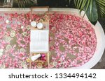 Top view of bath tub with flower petals and lemon slices. Book, candles and beauty product on a tray. Organic spa relaxation in luxury Bali outdoor bathroom.