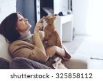 Young woman wearing warm sweater is resting with a cat on the armchair at home one autumn day