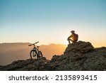 Cyclist mtb biker sits and relax on mountain top at sunset