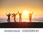 Group of happy tourists are having fun and dance at sunrise on mountain top over clouds