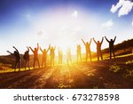Big group of happy friends stands on sunset backdrop with raised arms together. Friendship or teamwork concept