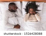 Small photo of Annoying snoring. Young black woman closing ears with hands suffering from loud snore of her sleeping husband.