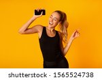 Music App. Sporty Woman In Wireless Earbuds Holding Smartphone And Dancing Over Yellow Background. Studio Shot